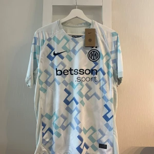 Inter Milan bortatröja Nike M - Inter Milan bortatröja från Nike i vitt med ljusblått och blått geometriskt mönster. Tröjan har korta ärmar, rund hals och klubbmärke samt Nike-logga på bröstet. Materialet är lätt och andas, perfekt för fotbollsträning eller match.