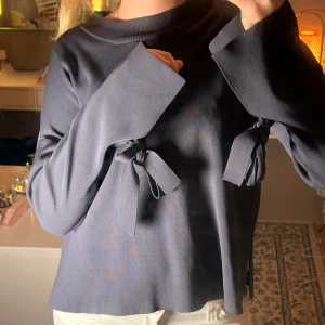 Mörkblå tröja med knyt  - Snygg mörkblå tröja från Wera med vida ärmar och coola knytband vid handlederna. Tröjan har en avslappnad passform och är tillverkad i mjukt material. Perfekt för dig som gillar unika detaljer och stilren design.