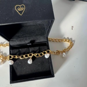 Pärlhalsband Guld - Snyggt halsband med chunky guldfärgad kedja och fem droppformade vita pärlor som hänger längs kedjan. Perfekt statement-piece som lyfter vilken outfit som helst. Kedjan har en trendig och modern vibe med sina stora länkar och pärldetaljer.