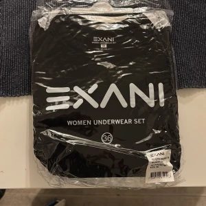 Svart underställstopp från Exani - Svart långärmad underställstopp från Exani i mjuk och stretchig polyesterblandning. Perfekt som baslager under kalla dagar. Enkel design utan synliga detaljer, rund hals och smidig passform.