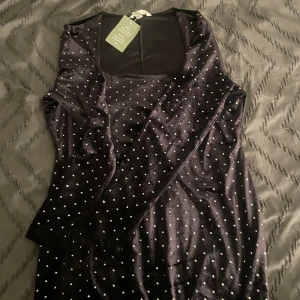 Svart glittrig prickig klänning H&M - Supersnygg svart klänning från H&M med glittrigt tyg och små vita prickar över hela. Klänningen har lång ärm, fyrkantig ringning och är gjord i mjuk, stretchig polyester. Perfekt för dig som vill sticka ut med en cool och trendig look.