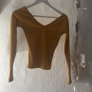 Ribbad gul långärmad topp Gina Tricot - Säljer en snygg ribbad topp från Gina Tricot i en djup gul färg. Modellen har lång ärm, v-ringad hals och är figurnära. Materialet är mjukt och stretchigt, perfekt för att ge en cool och trendig look. Passar dig som gillar stilrena detaljer och färg.