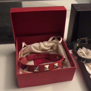 Rött Valentino armband med nitar - Säljer ett snyggt rött armband från Valentino med silvriga pyramidformade nitar. Armbandet är gjort i skinn och har ett justerbart spänne. Skicket är sådär men går enkelt att fixa✌️Bara att fråga om fler bilder! 