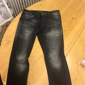 Svarta slim fit jeans Jack & Jones 29/30 - Snygga svarta slim fit jeans från Jack & Jones i storlek 29/30. Jeansen har slitna detaljer och en tvättad look med ljusare partier på lår och knän. Klassisk femficksmodell och smal passform som sitter tajt hela vägen ner. Bra skick 
