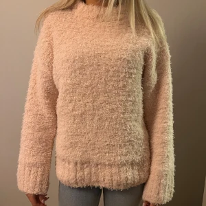 Rosa fluffig stickad tröja - Supermjuk och fluffig stickad tröja i ljusrosa ton. Tröjan har lång ärm, rak passform och hög hals. Perfekt för dig som vill ha en mysig och trendig look under kyliga dagar💕