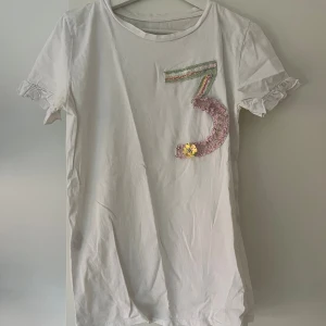 Vit t-shirt med paljettdekor och volang - Vit t-shirt med korta ärmar och volangdetaljer vid ärmsluten ❤️‍🔥