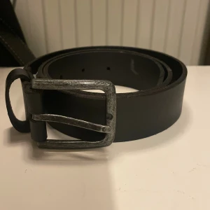 Svart skärp i skinn med metallspänne - Bälte som jag säljer pga storleken. Den är 75 cm lång 