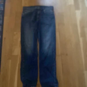 Blå jeans från Replay, storlek 12A - Snygga blå jeans från Replay i klassisk femficksmodell. Jeansen har raka ben och normal passform, med tydliga slitningar för en cool look. Materialet är slitstarkt denim och midjan är midwaist. Perfekt för dig som gillar stilrena och tidlösa jeans.