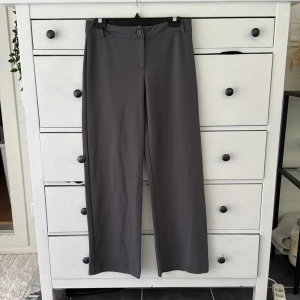 Grå kostymbyxor från Nelly, storlek M - Snygga grå kostymbyxor som är lågmidjade från Nelly i storlek M. Byxorna har raka ben, bälteshällor och stängs med knapp och dragkedja. Perfekta för en clean och stilren look. Materialet känns mjukt och följsamt.