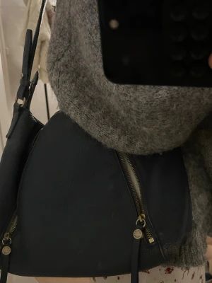 Svart axelväska i skinn från Radley - Snygg svart axelväska i äkta skinn  Väskan har två dragkedjor framtill med dekorativa detaljer och justerbar axelrem. Invändigt finns ett ljust foder och innerfack med dragkedja. Perfekt storlek för vardagens essentials.
