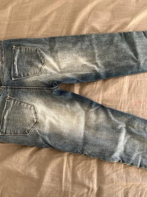 Blå straight fit jeans med slitningar - Snygga blå jeans med slitningar och tvättade detaljer. Klassisk femficksmodell med raka ben och kontrastsömmar. Perfekta för en avslappnad look och passar till det mesta. Materialet är tåligt denim i bomull.