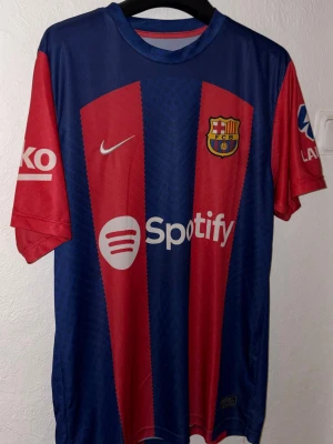 FC Barcelona matchtröja Nike blå/röd - Säljer en officiell FC Barcelona matchtröja från Nike i blått och rött med klubbmärke, Nike-logga och Spotify som sponsortryck. Tröjan har korta ärmar, rund hals och är tillverkad i ett lätt, ventilerande material perfekt för fotboll eller träning.