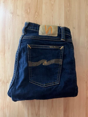Nudie jeans  - Marinblåa nudie jeans i modellen skinny lin. Midja 34cm, längd 97cm. JAG SKICKAR EJ FLER BILDER NÄR JAG BÄR JEANSEN! för bättre inblick i passformen rekommenderar jag att googla på modellnamnet. För storleksguide kolla måtten noggrant då jeansen alltid kan vara uppsydda heller krympta och jag ej tar emot returer :) s6,2