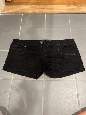 Svarta lågmidjade  jeansshorts från Bershka Denim - Svarta jeansshorts från  Bershka Denim. Modellen är lågmidjad och har knapp- och dragkedjestängning framtill. Perfekta för varma dagar och enkel att matcha med olika toppar.