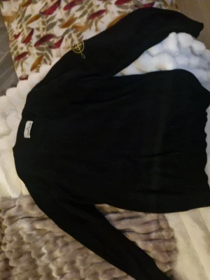 Svart stickad tröja Stone Island - Svart långärmad tröja från Stone Island med klassisk rund hals och ikonisk logga på ärmen. Tillverkad i mjukt material som känns skönt mot huden. Perfekt för dig som gillar stilrena och tidlösa plagg. Har använt den 1 gång.