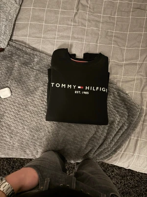 Svart sweatshirt Tommy Hilfiger - Snygg svart sweatshirt från Tommy Hilfiger med klassisk logga och texten 'EST. 1985' på bröstet. Tröjan har rund halsringning och soprena muddar vid ärmslut och nederkant. Perfekt för en avslappnad och stilren look.