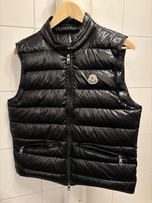 Moncler Gui Väst  - Säljer min Moncler Gui väst, mycket bra sick, enda defekten är en liten liten reva som syns på bild . Man kan självklart scanna märket som syns på sista bilden ✅ Vid ytterligare frågor är det bara att skriva👌