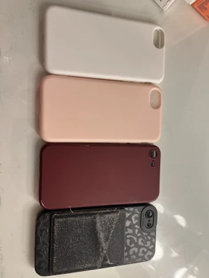 Fyra iPhone skal i olika färger - Säljer fyra snygga mobilskal till iPhone. Ett vitt, ett ljusrosa, ett vinrött och ett svart med leopardmönster och kortfack. Skalen är i plast eller silikon och har öppningar för kamera och knappar. Perfekt för dig som vill byta stil på mobilen!