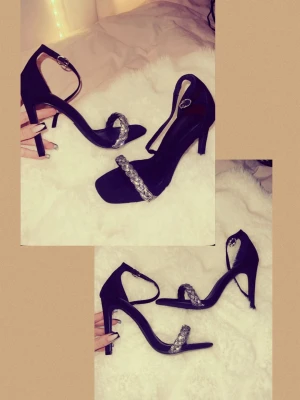Svarta klackar med glitter detalj - Säljer ett par svarta mocka klackar med hög klack och öppen tå. Skorna har en glittrig rem med strass över tårna och en smal ankelrem med spänne. Alldrig använda och skickas i orginal paketet! 💛💛Ordinarie pris 749kr!(: