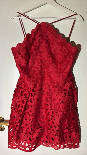 Röd spetsklänning från Chi Chi London - Supersnygg röd kort klänning från Chi Chi London Petite med tunna axelband och detaljerad spets i blommigt mönster. Klänningen har en omlottliknande överdel och är perfekt för dig som vill sticka ut med en elegant look.