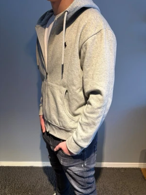 Ralph Lauren hoodie - Snygg grå hoodie från Ralph Lauren med dragkedja framtill och klassisk huva med dragsko.  Storlek M.  Modellen på bilden är 184.
