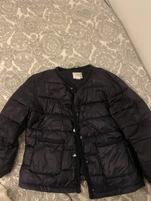 Svart pufferjacka från Gina Tricot - Snygg svart pufferjacka från Gina Tricot med tryckknappar framtill och två stora fickor. Perfekt till våren 