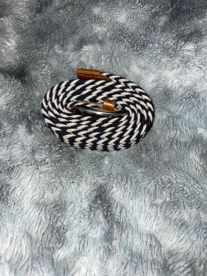 Marinblått och vitt flätat bälte - Snyggt flätat bälte i marinblått och vitt med detaljer i brunt läder och metallspänne. Bältet har ett coolt mönster och passar perfekt till jeans eller chinos. Märkt med VB på läderdetaljen för extra stilpoäng.