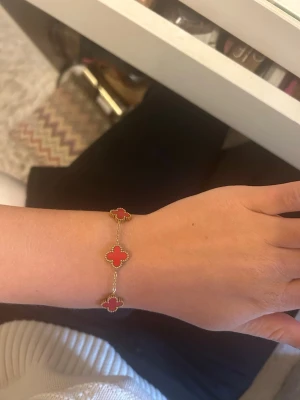 Guldarmband med röda clover-detaljer - Snyggt armband i guld med tre fyrklöverformade hängen i röd sten, omgivna av guldfärgade kanter. Gått i födelsedagspresent och aldrig använt, de är stainless steel🥰