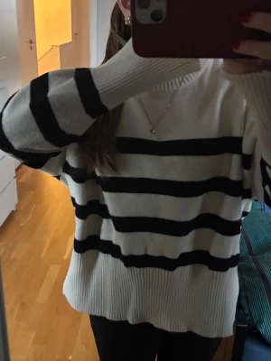 Vit stickad tröja med svarta ränder - Säljer en oversized vit stickad tröja med breda svarta horisontella ränder. Tröjan har rund halsringning och långa ärmar med ribbstickade muddar och nederkant. Perfekt för en avslappnad och trendig look.