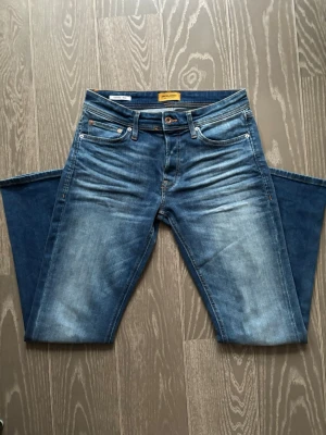 Blå jeans från Jack & Jones - Snygga blå jeans från Jack & Jones med klassisk femficksdesign och slitna detaljer framtill. Jeansen är precis köpta men kom inte till användning så säljer de. Nypris ligger på under tusenlappen. Mitt pris 689 vilket är riktigt schysst. Hör av vid funderingar!