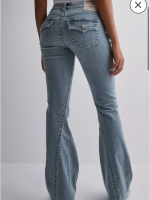 Ljusblå bootcut jeans True Religion - Säljer ett par ljusblå bootcut jeans från True Religion med ikoniska bakfickor och silverfärgade knappar. Jeansen har låg midja och klassisk femficksdesign. Materialet är mjukt denim i bomull och passformen är loose med utsvängda ben. 27 x 32