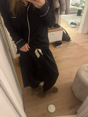 Mörkblå pyjamas med ljusrosa detaljer - Snygg mörkblå pyjamas med ljusrosa kontrastsömmar och knappar. Setet består av långärmad skjorta och byxor. Perfekt för mysiga kvällar hemma. Materialet är i stain o säljer då den tyvärr inte kommer till användning. Köpt för ca 1000 kr på BlueBella för några år sedan