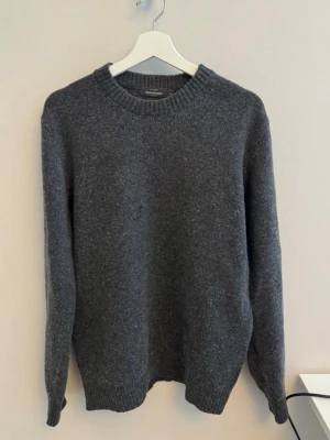 Stickad ulltröja - Säljer en mörkgrå stickad ulltröja från Dressman i Storlek M. Tröjan är i nyskick och använd endast ett fåtal gången. Köpt i november 2025 för 700 kr. Kvitto medföljer.