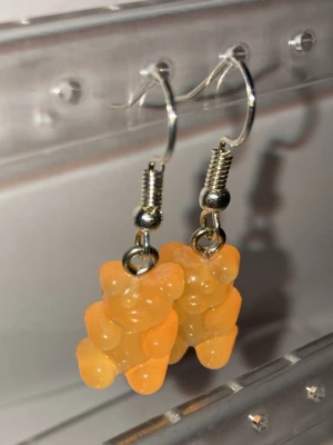 Orange björngodis örhängen - Handgjorda söta örhängen med hängen formade som orangea gelégodisbjörnar. Hängena är gjorda i plast och sitter på silvriga krokar. Perfekta för dig som gillar lekfulla och färgglada accessoarer. Frakt 22-100kr. Kontakta mig om du vill köpa eller har frågor.