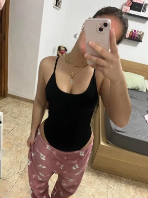 Svart ribbad bodysuit med smala axelband - Svart bodysuit med smala justerbara axelband och v-ringad halsringning. Tillverkad i ribbad stretchig syntet som formar kroppen. Perfekt att styla med jeans eller kjol.