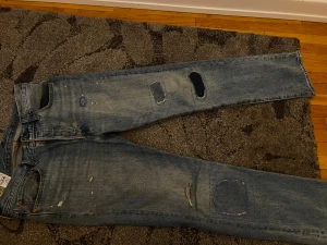 Levi's 501 ljusblå jeans med patchar - Ljusblå Levi's 501 jeans med raka ben och flera patchade hål och slitningar för en riktigt vintage vibe. Klassisk femficksmodell med knappgylf och detaljer i koppar. Perfekta för dig som gillar en avslappnad och unik stil.