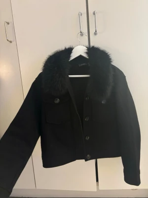 Svart pälsjacka med krage - Snygg svart pälsjacka med fluffig krage och knappar framtill. Samt 2 fickor framtil där man kan förvara telefon osv. Perfekt för dig som vill ha en stilren och cool jacka till höst och vinter. Jackan är lite nopprig och man kan hitta hår för det finns katt i hemmet! Innan jag skickar kommer jag försöka få bort det m mesta med noppermaskin samt roller! Jag har sytt dit pälsen själv och den liknar meotie jackorna som kostar 3000kr!😍