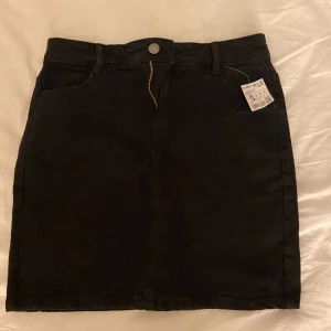 Svart kortkjol från KappAhl - Svart kortkjol från KappAhl med klassisk jeanslook, fickor fram . Kjolen har dragkedja och knapp framtill. 