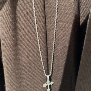 Silverfärgat  korshalsband - Snyggt halsband i silverfärg med. Kedjan är tvinnad och ger en cool touch, medan hänget har en glittrig yta som gör det extra iögonfallande. Perfekt för dig som gillar unika smycken.