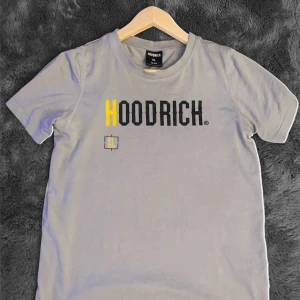 Grå HOODRICH t-shirt med tryck XL - Snygg grå t-shirt från HOODRICH i storlek XL, med coolt tryck både fram och bak i svart och gult. Klassisk passform och rund hals. Tillverkad i mjuk bomull som är skön att ha på sig hela dagen. Perfekt för dig som gillar streetwear vibes.