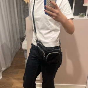 Svart axelväska från Gina Tricot - Svart axelväska med flera fack och silvriga dragkedjor från Gina Tricot. Väskan har en justerbar axelrem och en extra rem med nitar för att byta stil. Perfekt storlek för mobilen, plånboken och smågrejer. Snygg och praktisk för dig som gillar att ha koll på dina saker.