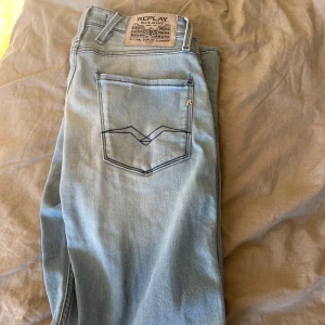 Replay Anbass ljusblå jeans W29 L32 - Säljer ett par Replay Anbass jeans i ljusblå tvätt. Klassisk femficksmodell med snygga detaljer på bakfickorna och Replay-märke i läder baktill. Jeansen är i stretchig bomull och har dragkedjegylf. Perfekta för dig som gillar en modern och avslappnad look.