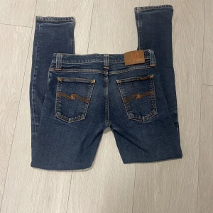 Mörkblå slim jeans från Nudie Jeans W29 L30 - Säljer ett par mörkblå jeans från Nudie Jeans med klassiska orange sömmar och snygga bakfickor med vågigt broderi. Modellen har slim passform. Perfekta för dig som gillar stilrena och tidlösa jeans. Nypris ca 1700