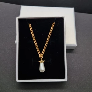 Guldfärgat halsband med pärlhänge - Stilrent halsband med en kedja i guldfärg och ett droppformat vitt pärlhänge. Kedjan har klassisk länkdesign och pärlan sitter fast i ett dekorativt fäste. Perfekt för dig som gillar en elegant och trendig look.