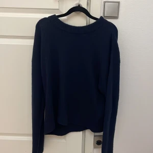 Mörkblå stickad tröja med rund hals - Mysig mörkblå stickad tröja med rundad hals och långa ärmar. Tröjan har ribbade detaljer vid halsringningen och ärmsluten, vilket ger en schysst och enkel look. Perfekt för dig som gillar basic och stilrena plagg.