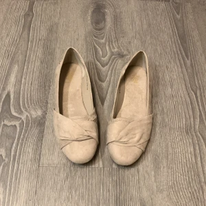 Ballerinaskor beige/grå - Ett par beige/gråa ballerinaskor i storlek 38. Stilrena skor med en fin snörning där fram, matta i färgen. Helt oanvända i nytt skick. Passar både till vardags eller om man vill klä upp sig!