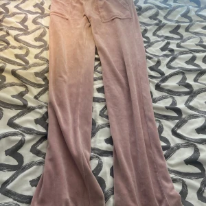 Rosa mjukisbyxor med fickor - Säljer ett par ljusrosa mjukisbyxor i mjukt material med två bakfickor med lock och knapp. Byxorna har en relaxed passform och vida ben, perfekta för en chill och avslappnad look.