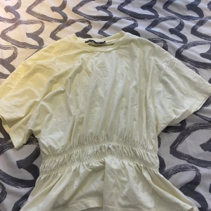 Ljusgul kortklänning med resårmidja - Säljer en ljusgul kortklänning från Monki med rund hals och korta ärmar. Klänningen har en snygg resår i midjan som ger en cool och avslappnad siluett. Perfekt för dig som gillar enkel och chill stil.
