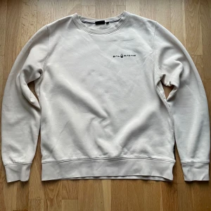 Beige Sail Racing sweatshirt L - Säljer en stilren beige sweatshirt från Sail Racing i storlek L. Tröjan har rund hals, mjukt bomullsmaterial och diskret logga på bröstet samt en liten logga i nacken. Perfekt för dig som gillar cleana och enkla plagg nu till hösten eller vintern.