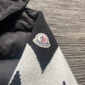Moncler Cardigan Tricot - Säljer en svart cardigan från Moncler med huva och dragkedja. Jackan har quiltad front i dun, stickade ärmar med vit blixtmönster och Moncler-logga på axeln. Snygga snören i huvan och ribbade muddar. Perfekt för dig som gillar streetstyle och exklusiva märken. Jackan är storlek S och är riktigt bra skick! Skriv vid funderingar eller fler bilder. Som vanligt är priset inte fast hugget i sten! Osäker på äktenhet dock!!!!